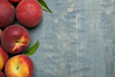 Photo of Fresh peaches and leaves on blue wooden table, top view with space for text