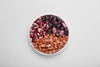 Photo of Different kinds of kidney beans in bowl on white background, top view