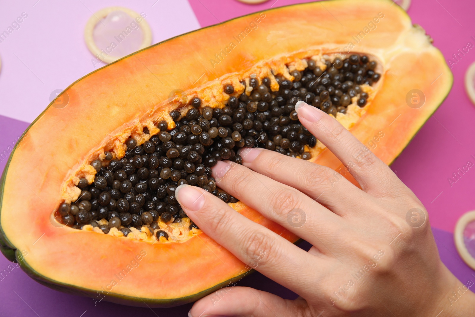 Photo of Young woman touching half of papaya and condoms on color background, closeup. Sex concept