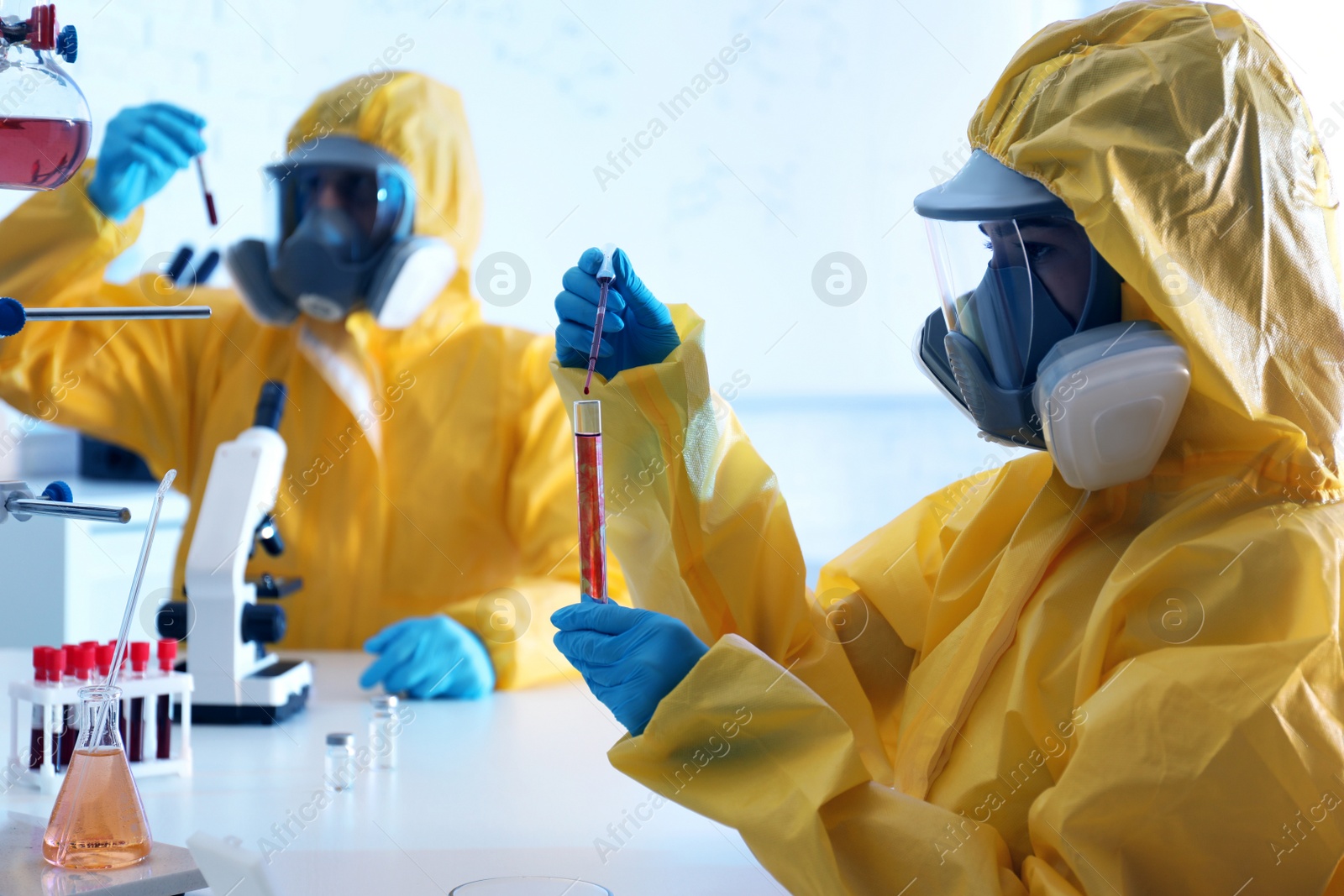 Photo of Scientist in chemical protective suit dripping blood  into test tube at laboratory. Virus research