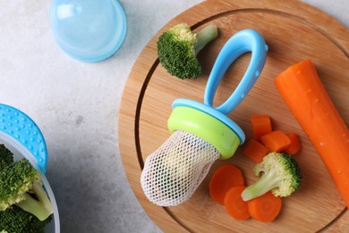 Photo of Nibbler with boiled broccoli and carrot on light grey table, flat lay. Baby feeder