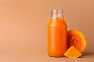 Photo of Tasty pumpkin juice in glass bottle and cut pumpkin on pale orange background. Space for text