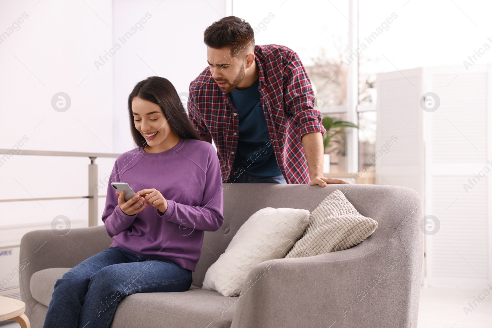 Photo of Distrustful young man peering into girlfriend's smartphone at home