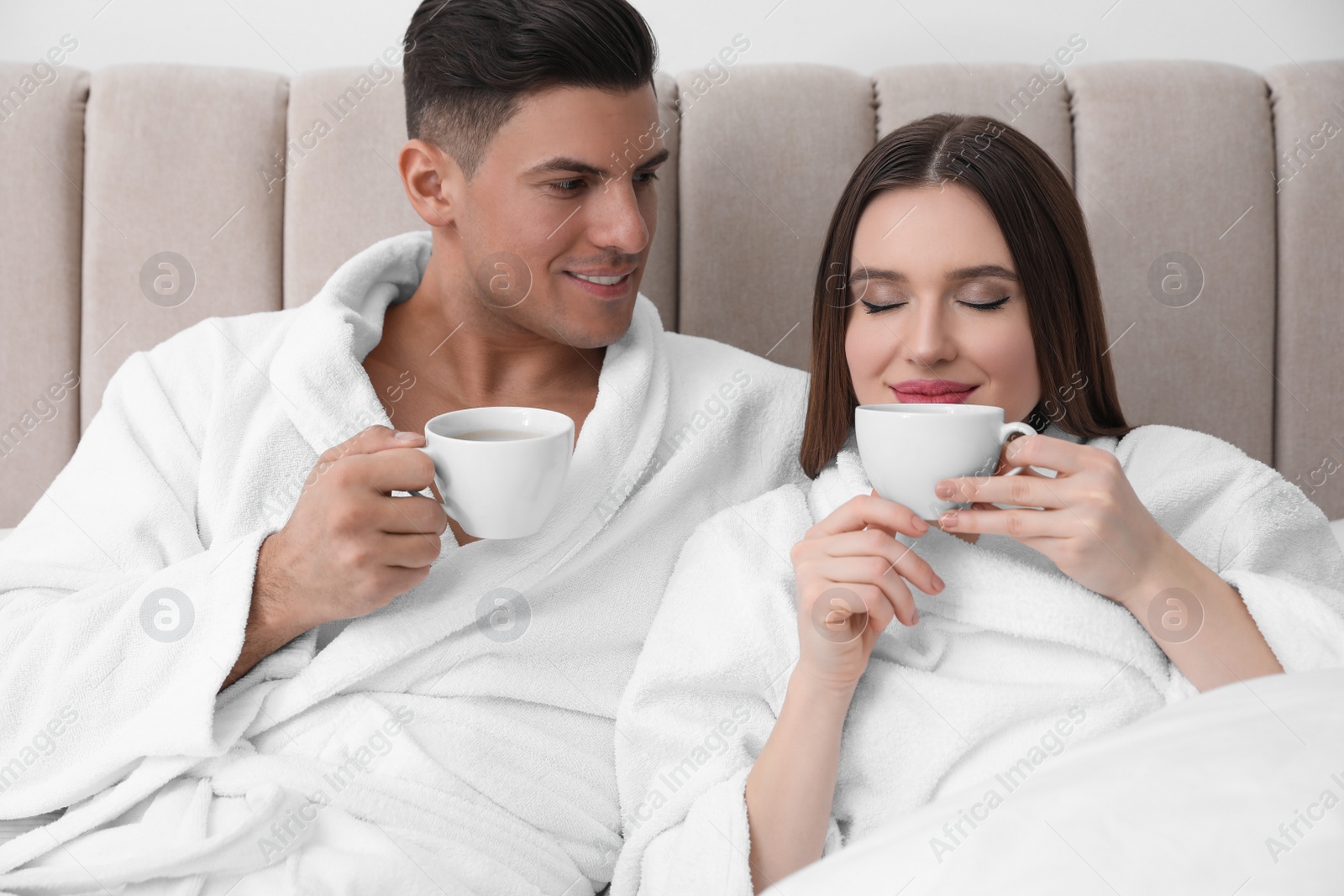 Photo of Happy couple in bathrobes with coffee on bed at home