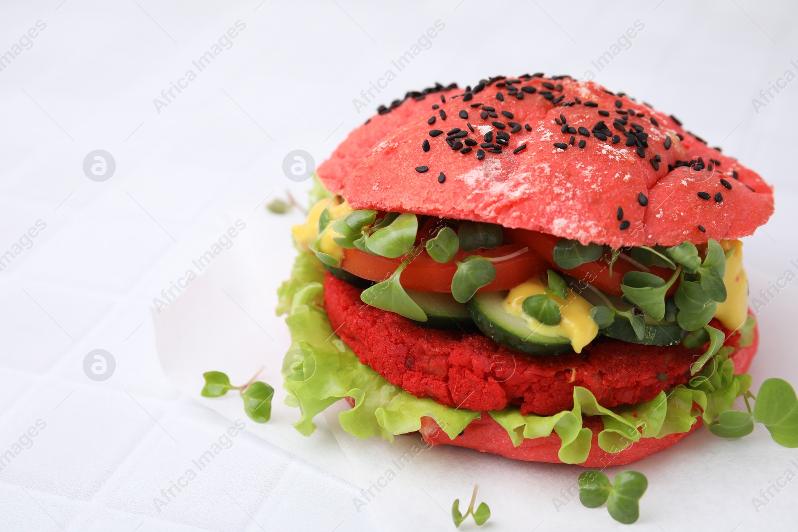 Photo of Tasty pink vegan burger with vegetables, patty and microgreens on white tiled table, closeup. Space for text