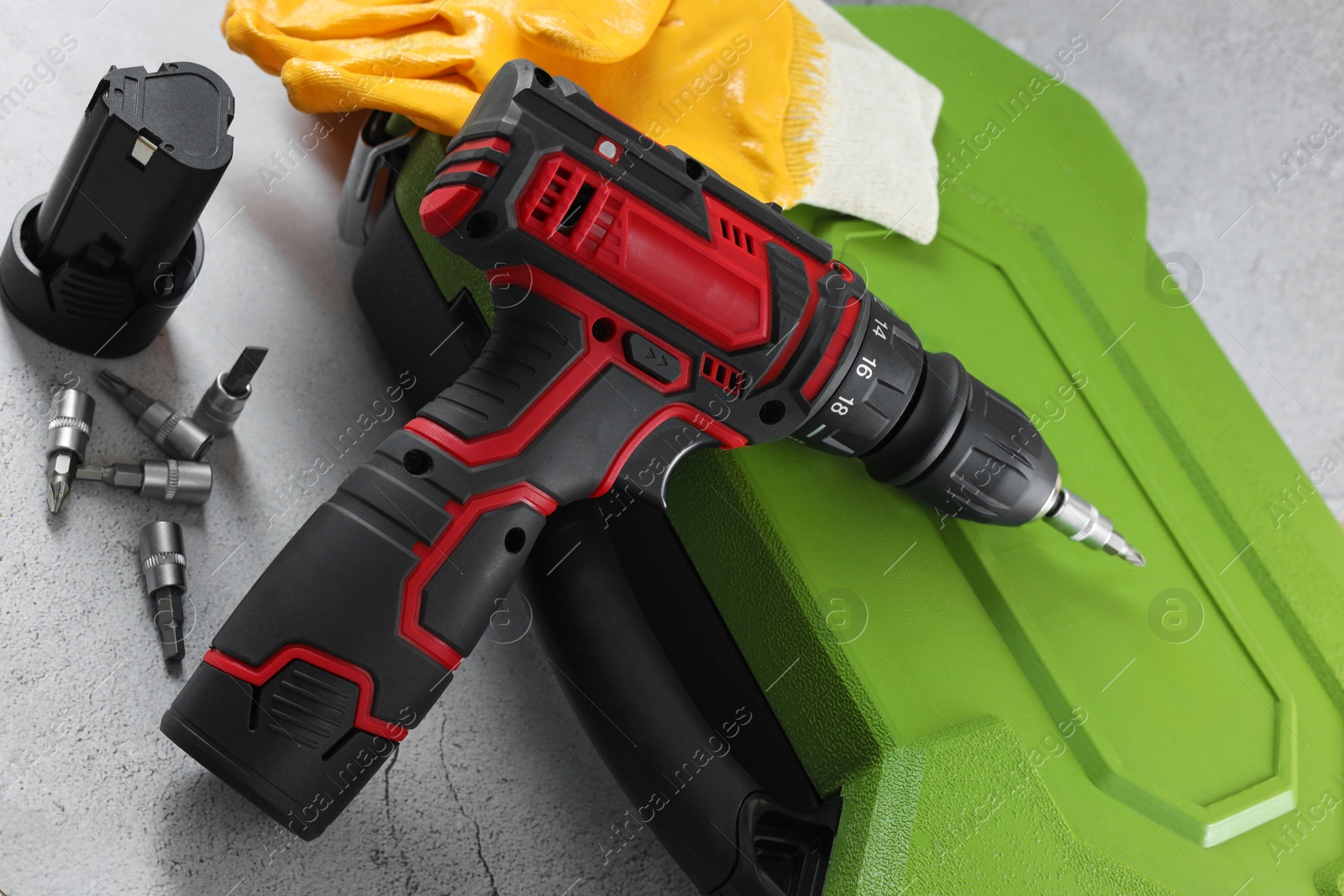 Photo of Electric screwdriver, case, drill bits, battery and gloves on light table, closeup