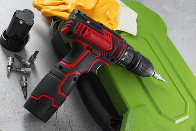 Electric screwdriver, case, drill bits, battery and gloves on light table, closeup