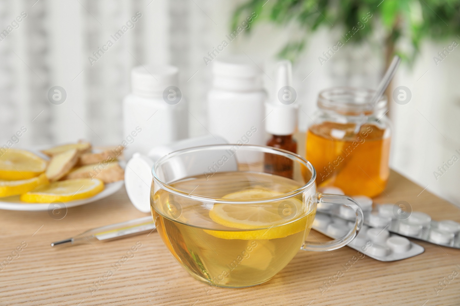 Photo of Glass cup of hot tea with lemon and different cold remedies on wooden table