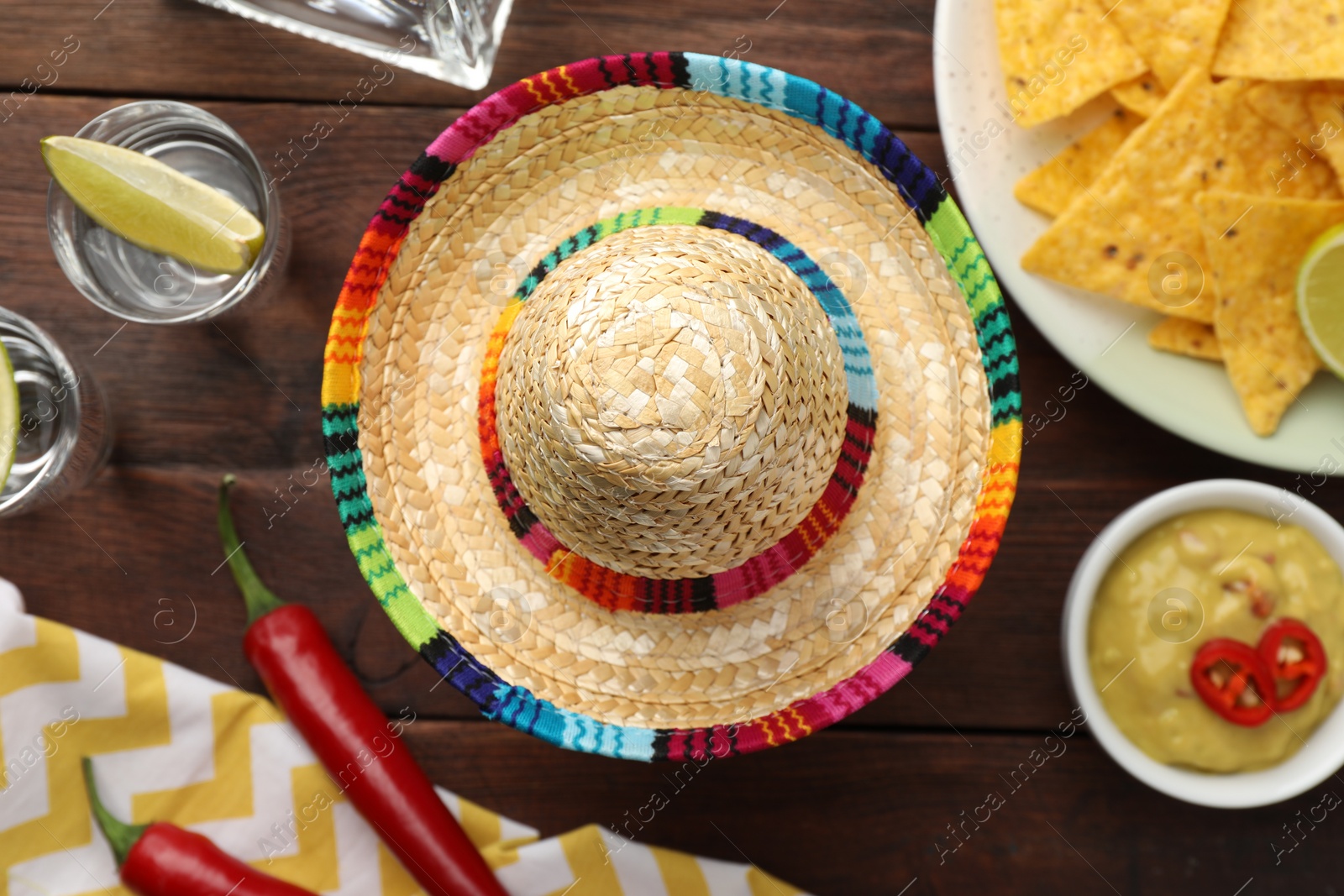 Photo of Mexican sombrero hat, tequila with lime, chili peppers, nachos chips and dip sauce on wooden table, flat lay