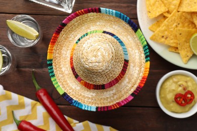 Photo of Mexican sombrero hat, tequila with lime, chili peppers, nachos chips and dip sauce on wooden table, flat lay