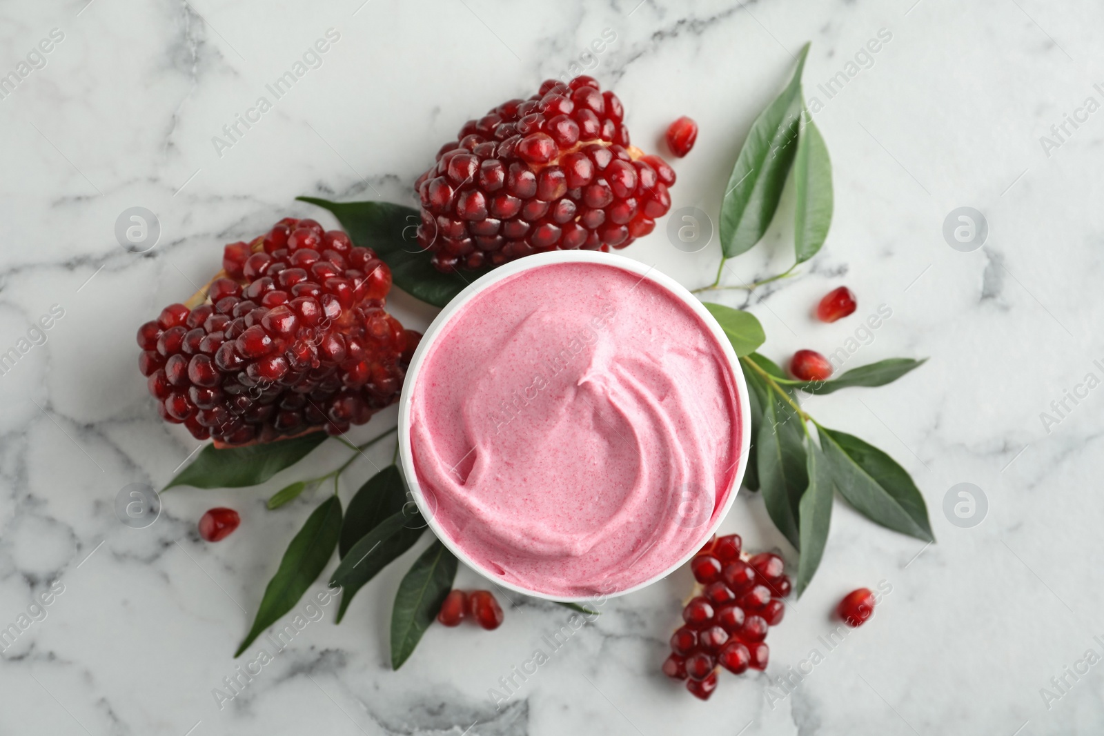 Photo of Fresh pomegranate and jar of facial mask on white marble table, flat lay. Natural organic cosmetics