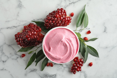 Fresh pomegranate and jar of facial mask on white marble table, flat lay. Natural organic cosmetics