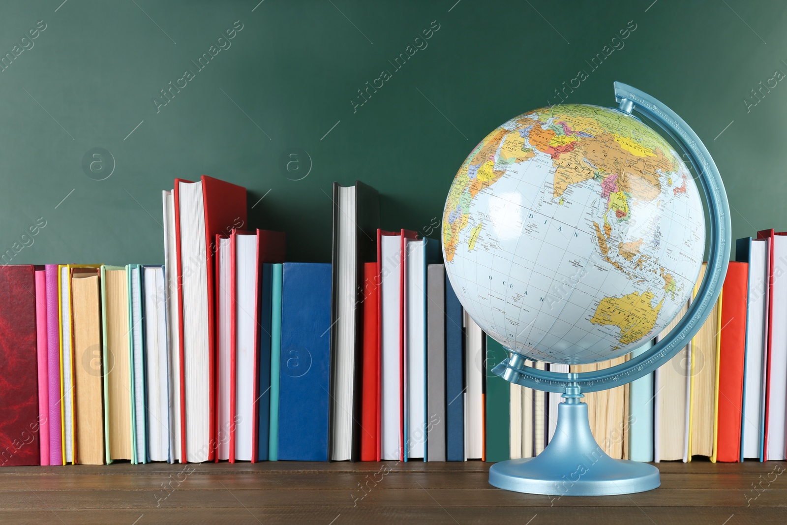 Photo of Globe and many books on wooden table near green chalkboard. Geography lesson