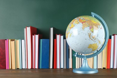 Globe and many books on wooden table near green chalkboard. Geography lesson