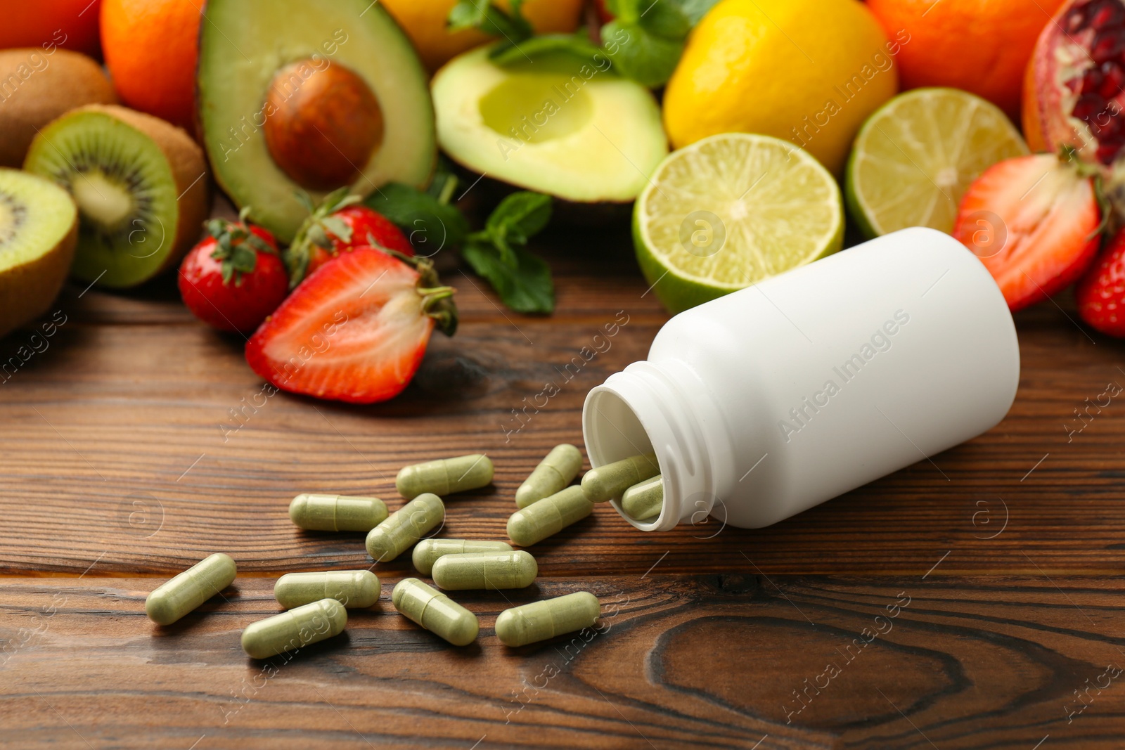 Photo of Vitamin pills, bottle and fresh fruits on wooden table