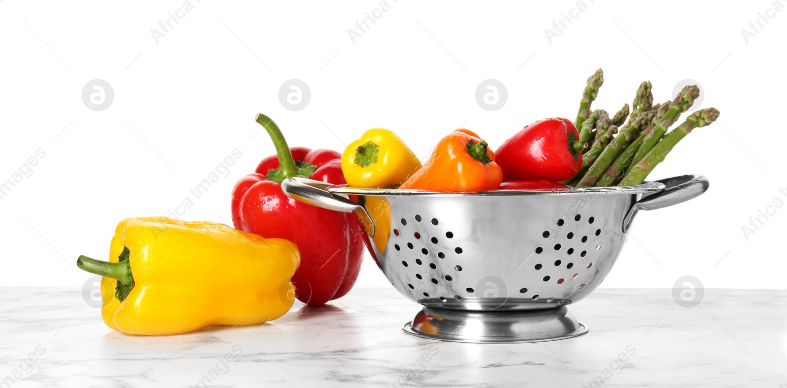 Photo of Metal colander with different vegetables on marble table against white background