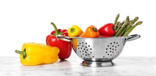 Photo of Metal colander with different vegetables on marble table against white background