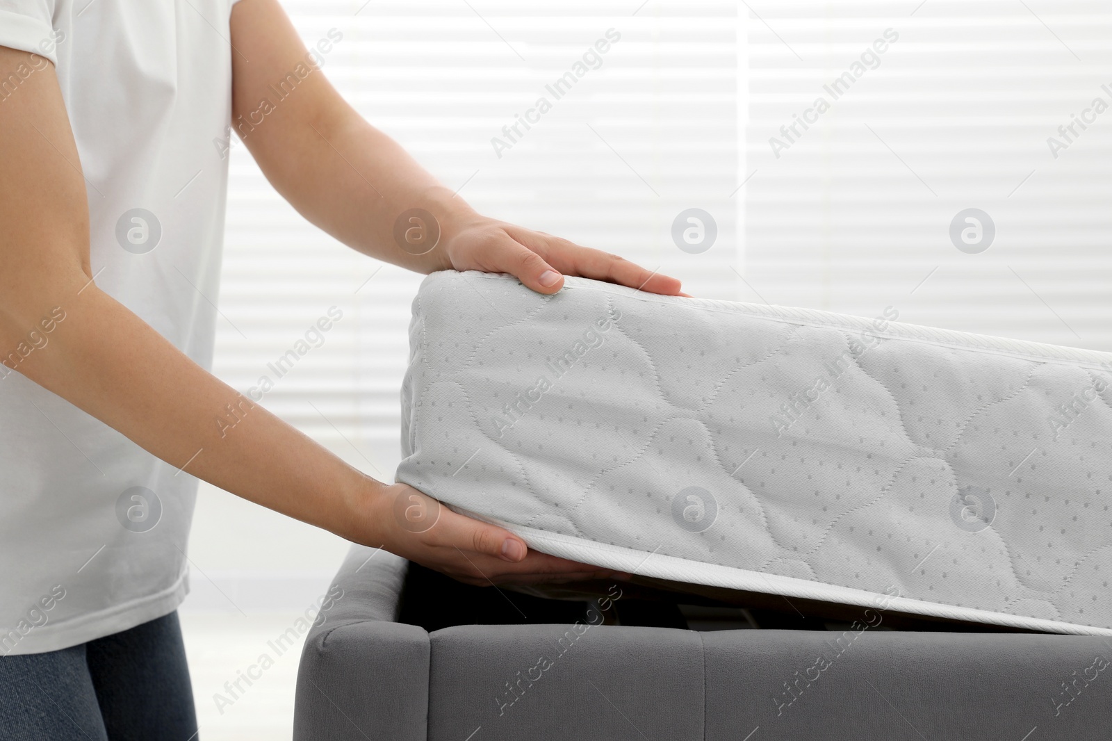 Photo of Woman putting soft light green mattress on gray bed indoors, closeup