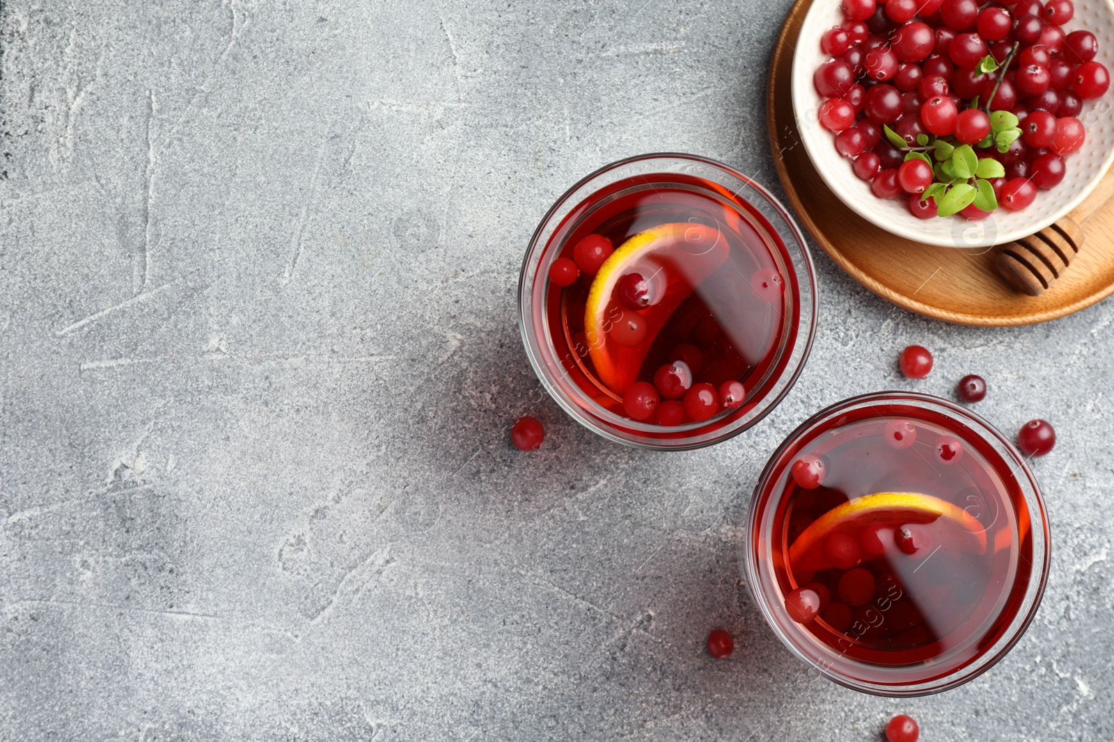 Photo of Tasty hot cranberry tea with lemon in glasses and fresh berries on light grey textured table