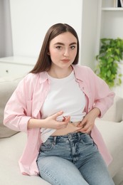 Photo of Diabetes. Woman making insulin injection into her belly on sofa at home