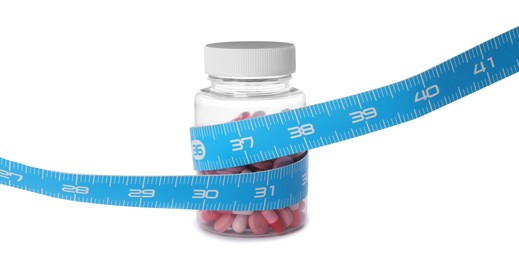 Jar of weight loss pills and measuring tape on white background