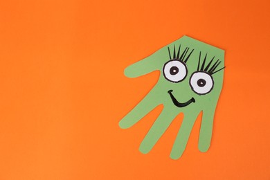 Photo of Funny green hand shaped monster on orange background, top view with space for text. Halloween decoration