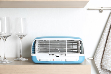 Photo of Modern air purifier and glasses on wooden shelf in kitchen