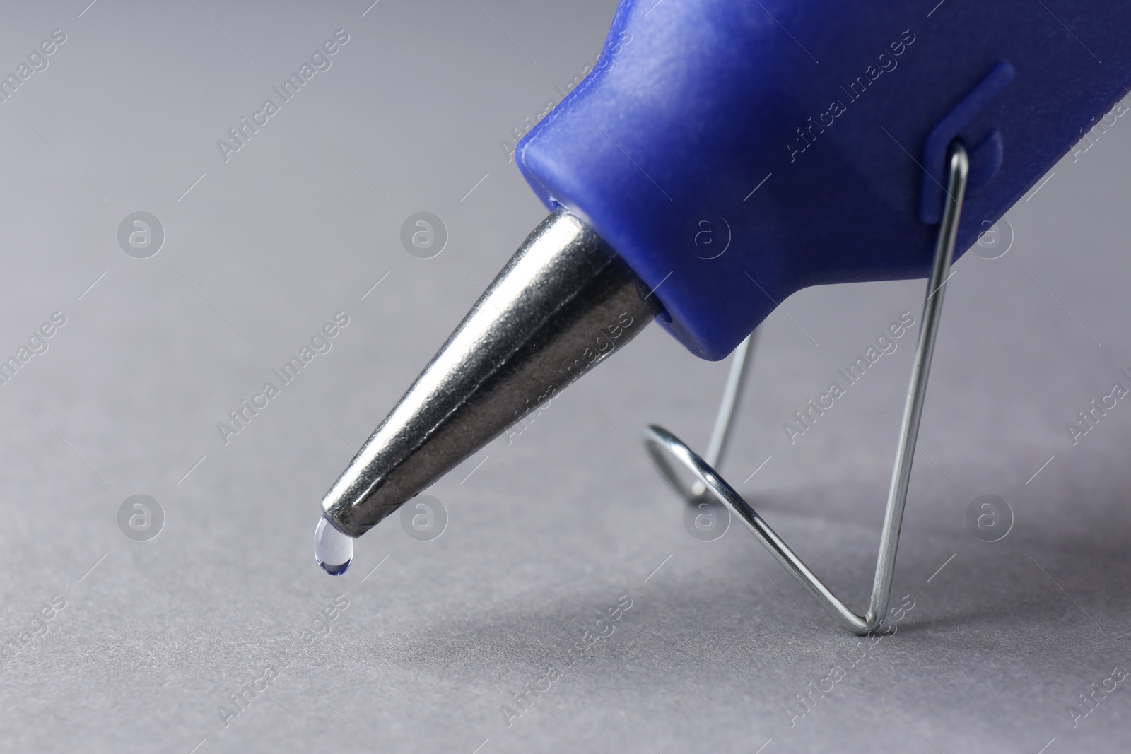 Photo of Melted glue dripping out of hot gun nozzle on grey background, closeup