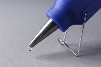 Photo of Melted glue dripping out of hot gun nozzle on grey background, closeup