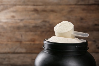 Black jar with measuring scoop of protein powder against wooden background. Space for text