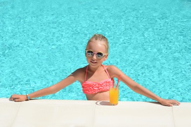 Photo of Cute little girl with glass of juice at swimming pool edge on sunny day