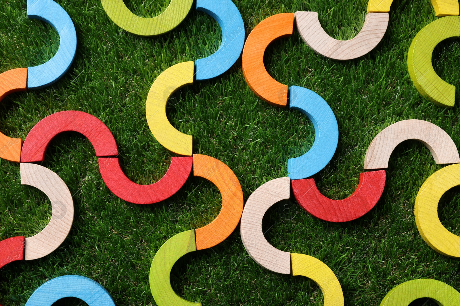 Photo of Colorful wooden pieces of play set on green grass, flat lay. Educational toy for motor skills development