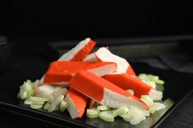 Photo of Fresh crab sticks with celery served on black plate, closeup