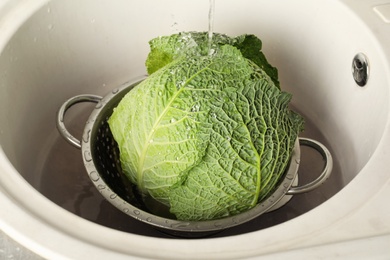 Photo of Washing savoy cabbage in colander under tap water