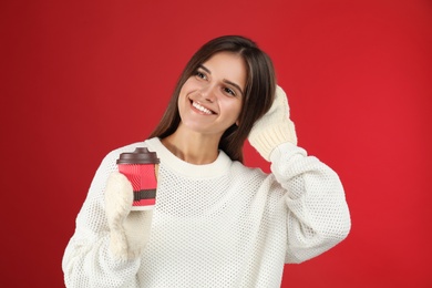 Happy beautiful woman with paper cup of mulled wine on red background