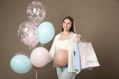 Happy pregnant woman with gifts and balloons near dark wall. Baby shower party