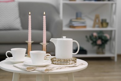 Photo of Cups of tea, teapot and burning candles on white coffee table indoors. Space for text