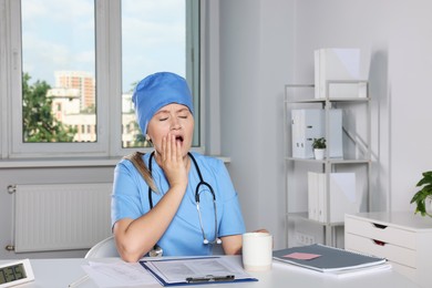 Photo of Tired young doctor yawning at workplace in office