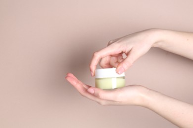 Woman with jar of cream on beige background, closeup