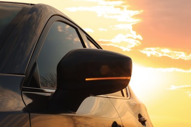Photo of Black modern car outdoors at sunset, closeup of side view mirror