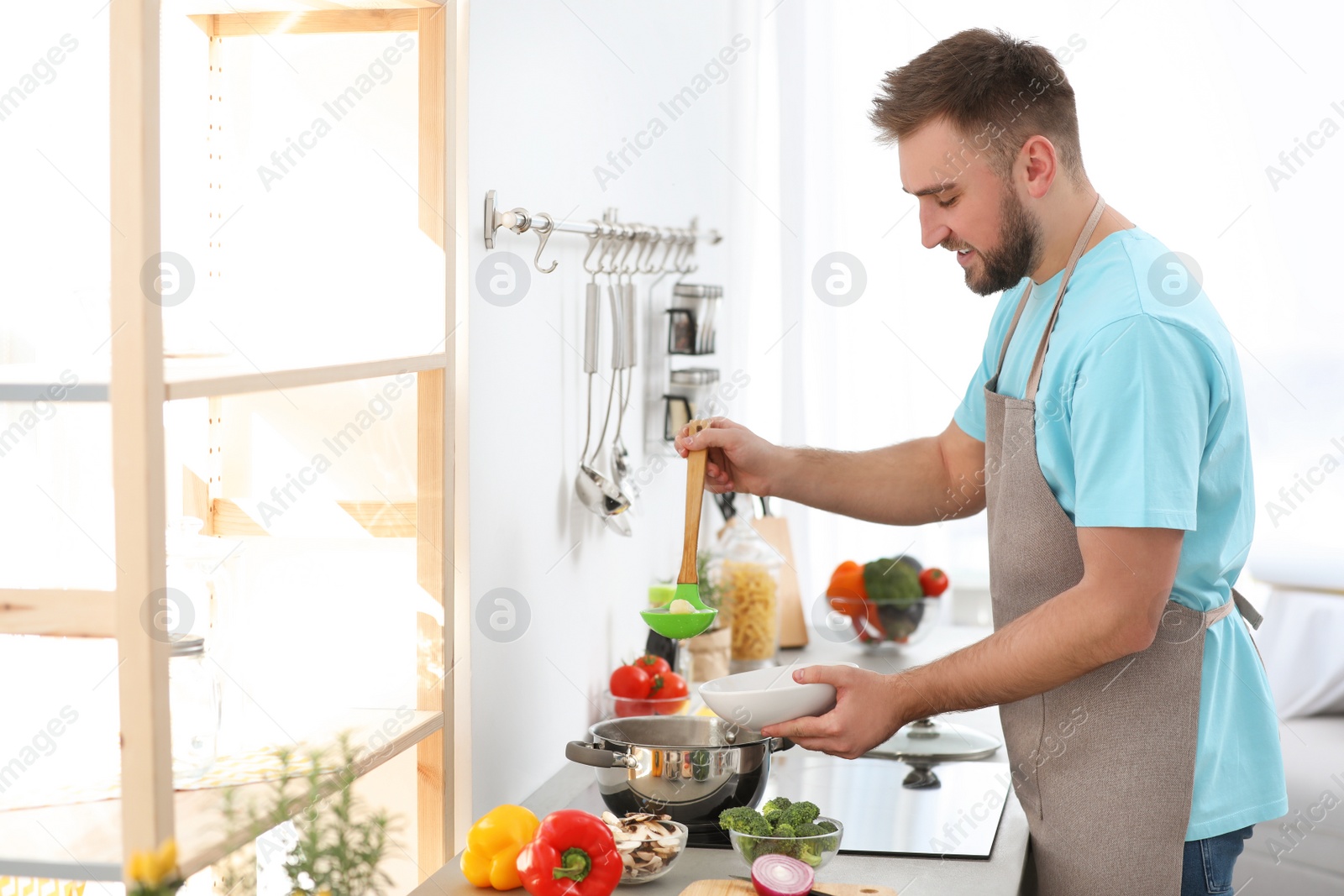 Photo of Young man pouring delicious soup into bowl at home