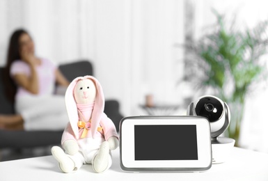 Photo of Baby monitor, camera with toy on table and woman resting in living room. Video nanny