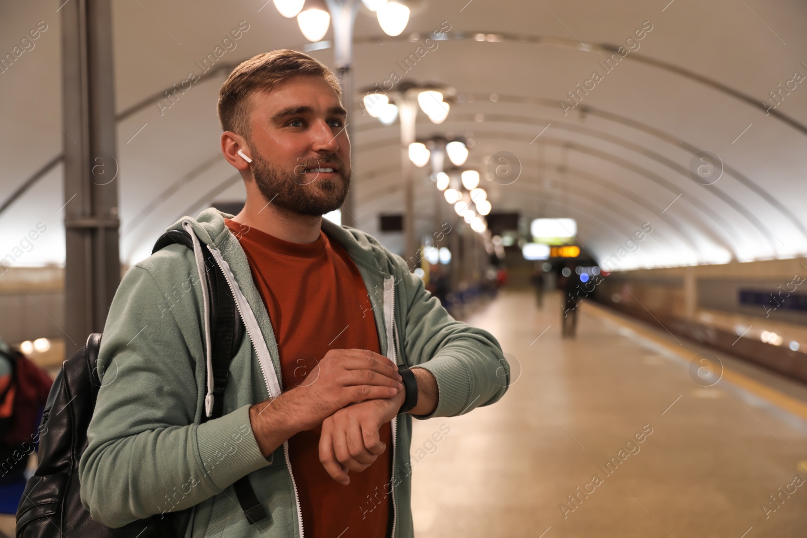 Photo of Young man with backpack and earphones waiting for train at subway station. Public transport