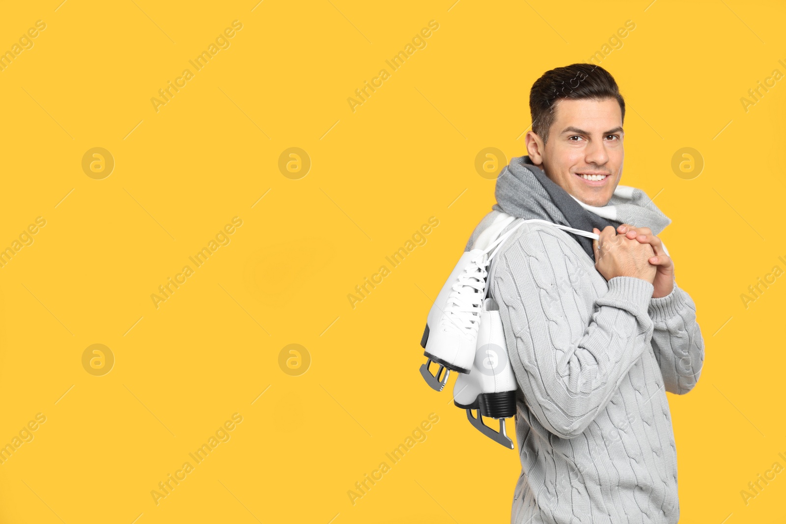 Photo of Happy man with ice skates on yellow background. Space for text