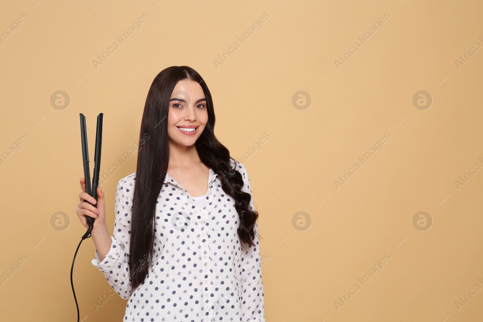 Photo of Beautiful happy woman with hair iron on beige background. Space for text