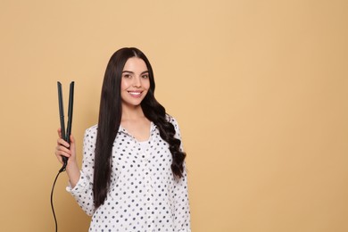 Beautiful happy woman with hair iron on beige background. Space for text