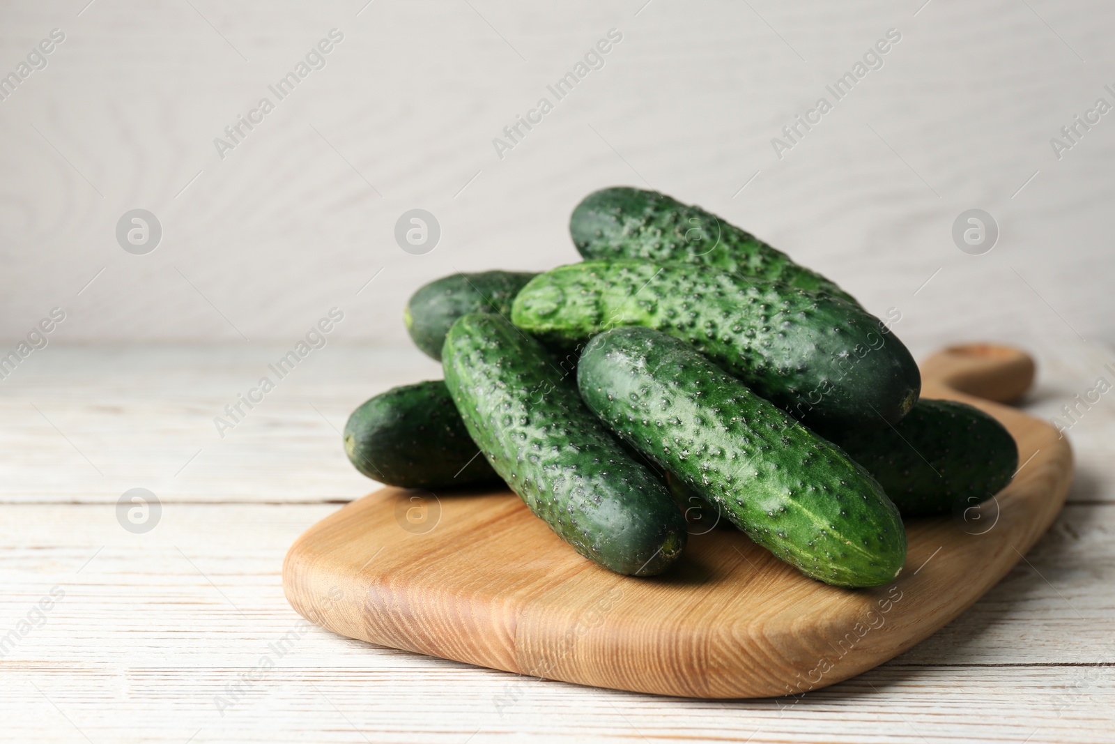 Photo of Board with fresh ripe cucumbers on white wooden table, space for text