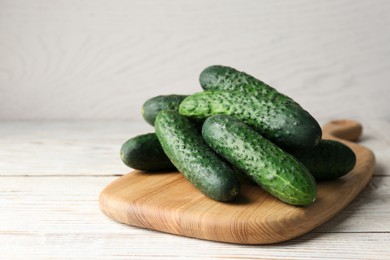 Board with fresh ripe cucumbers on white wooden table, space for text