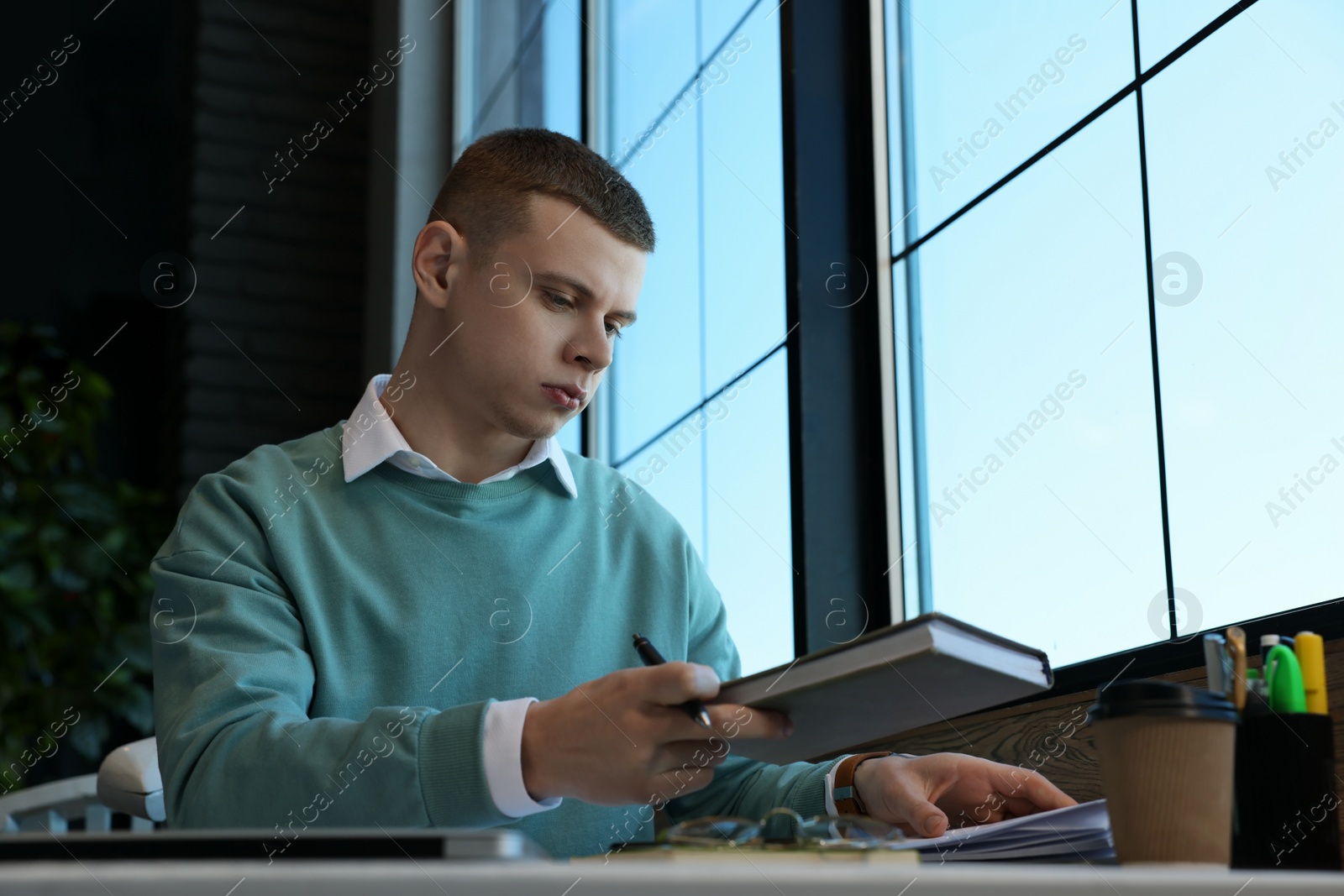 Photo of Young male student with notebooks studying at table in cafe