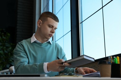 Young male student with notebooks studying at table in cafe